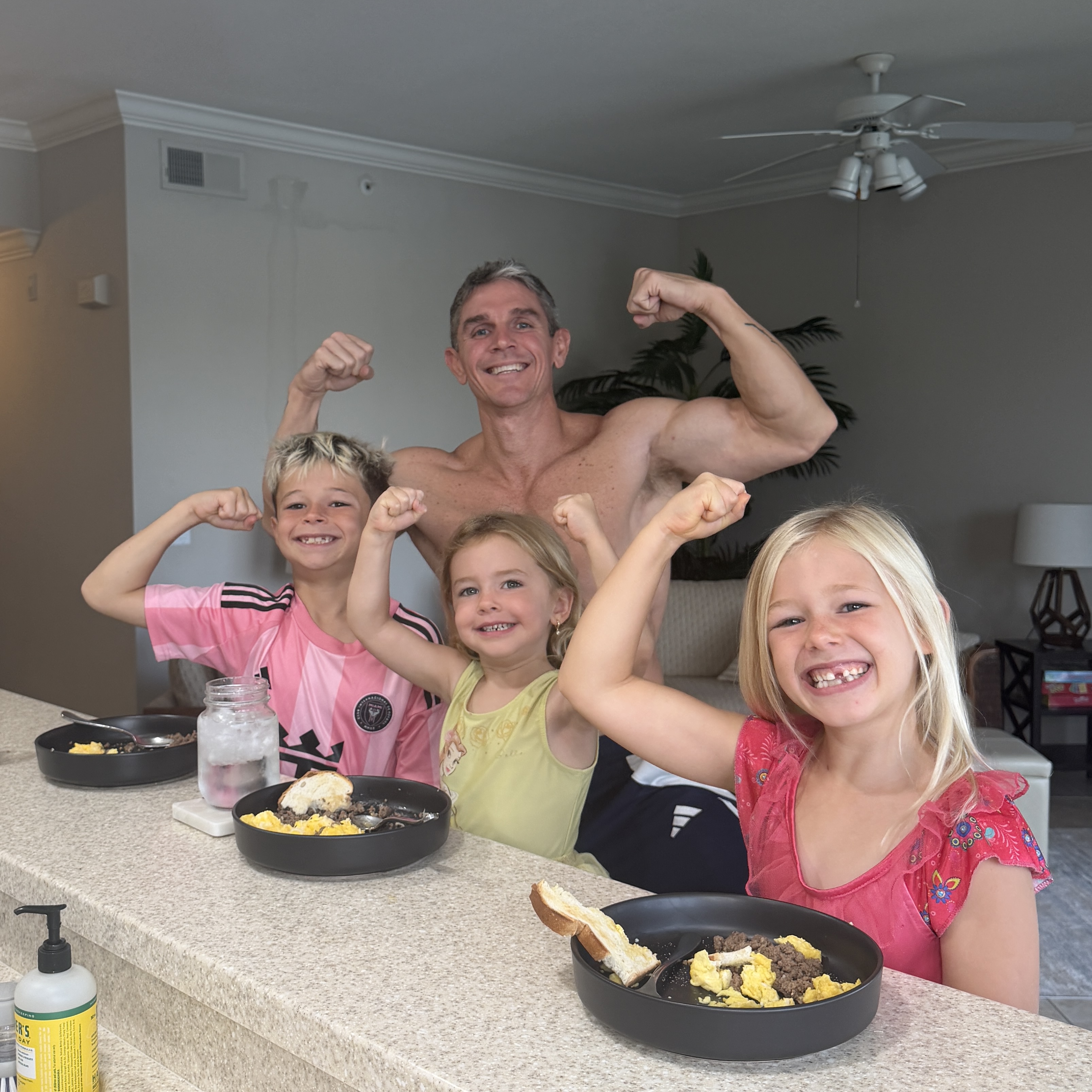Jason Wittrock and his three kids flexing their arms and smiling at the breakfast counter